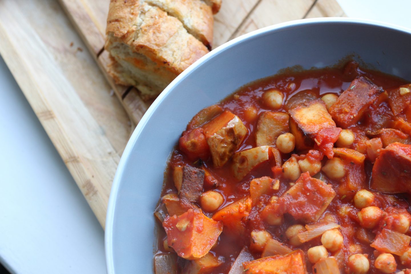 bowl of rustic winter vegetable casserole next to some garlic baguette on a wooden tray