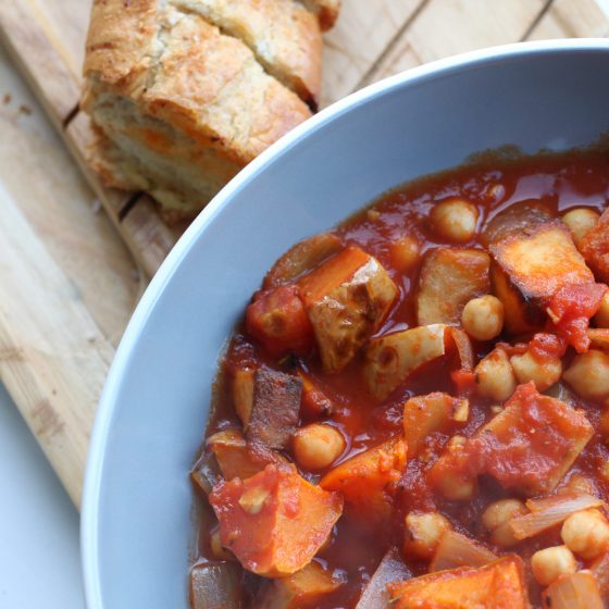 bowl of rustic winter vegetable casserole next to some garlic baguette on a wooden tray