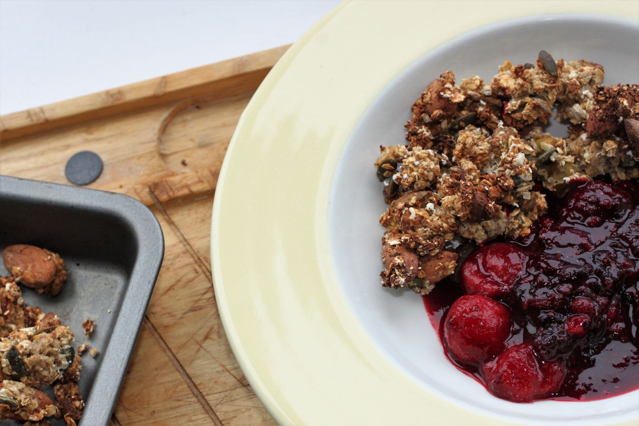 refined sugar free nutty granola in a bowl with some berry compote on a wooden tray