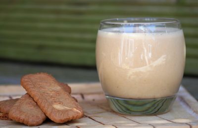 glass of biscoff milkshake on a wooden board, next to some biscoff biscuits. The tray is resting on an outdoor wooden bench.