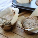 two muffins in cases on a wooden tray with a cream tea towel in the background