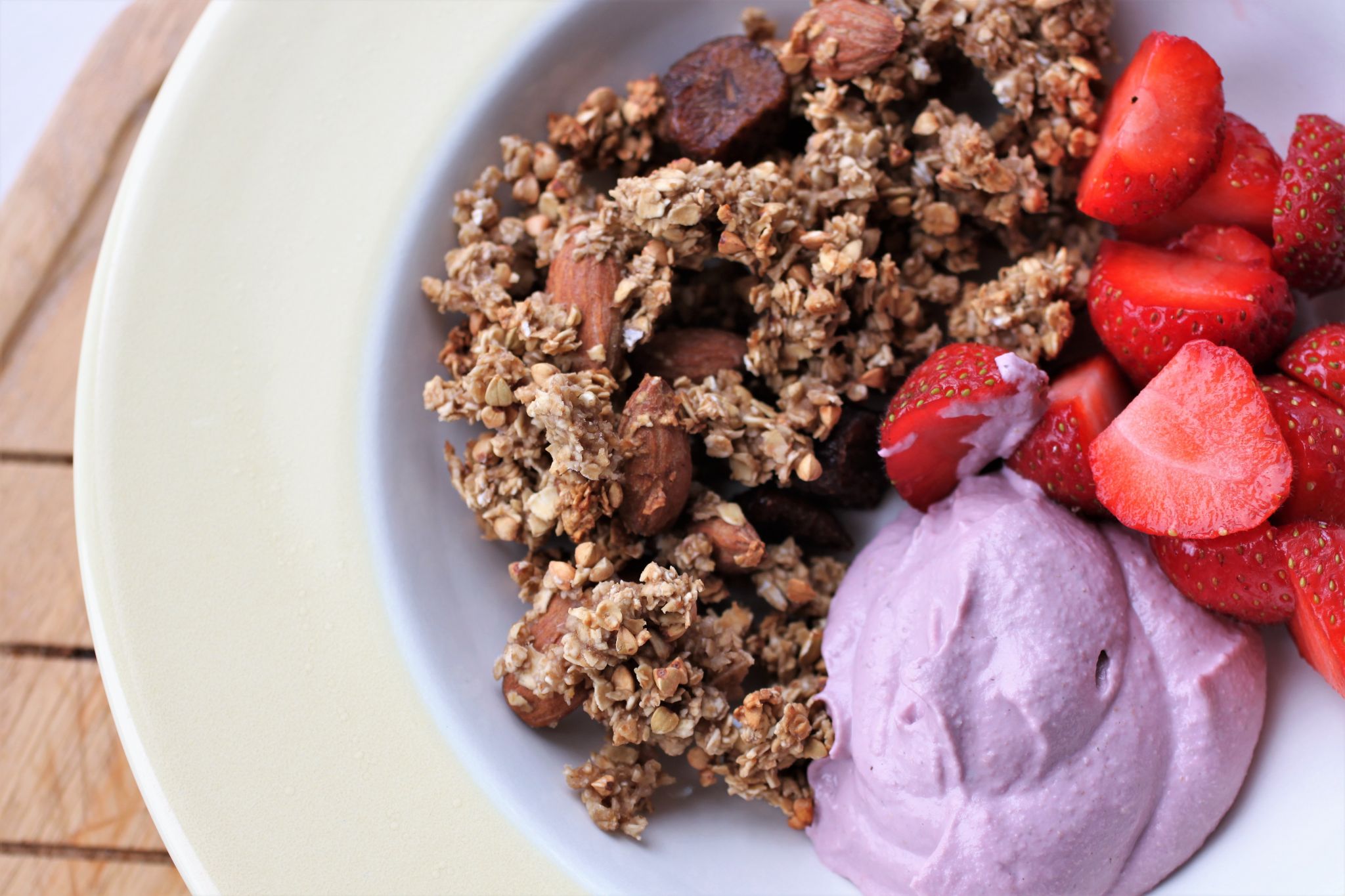 strawberry granola in a bowl with some strawberry cashew cream and fresh strawberries