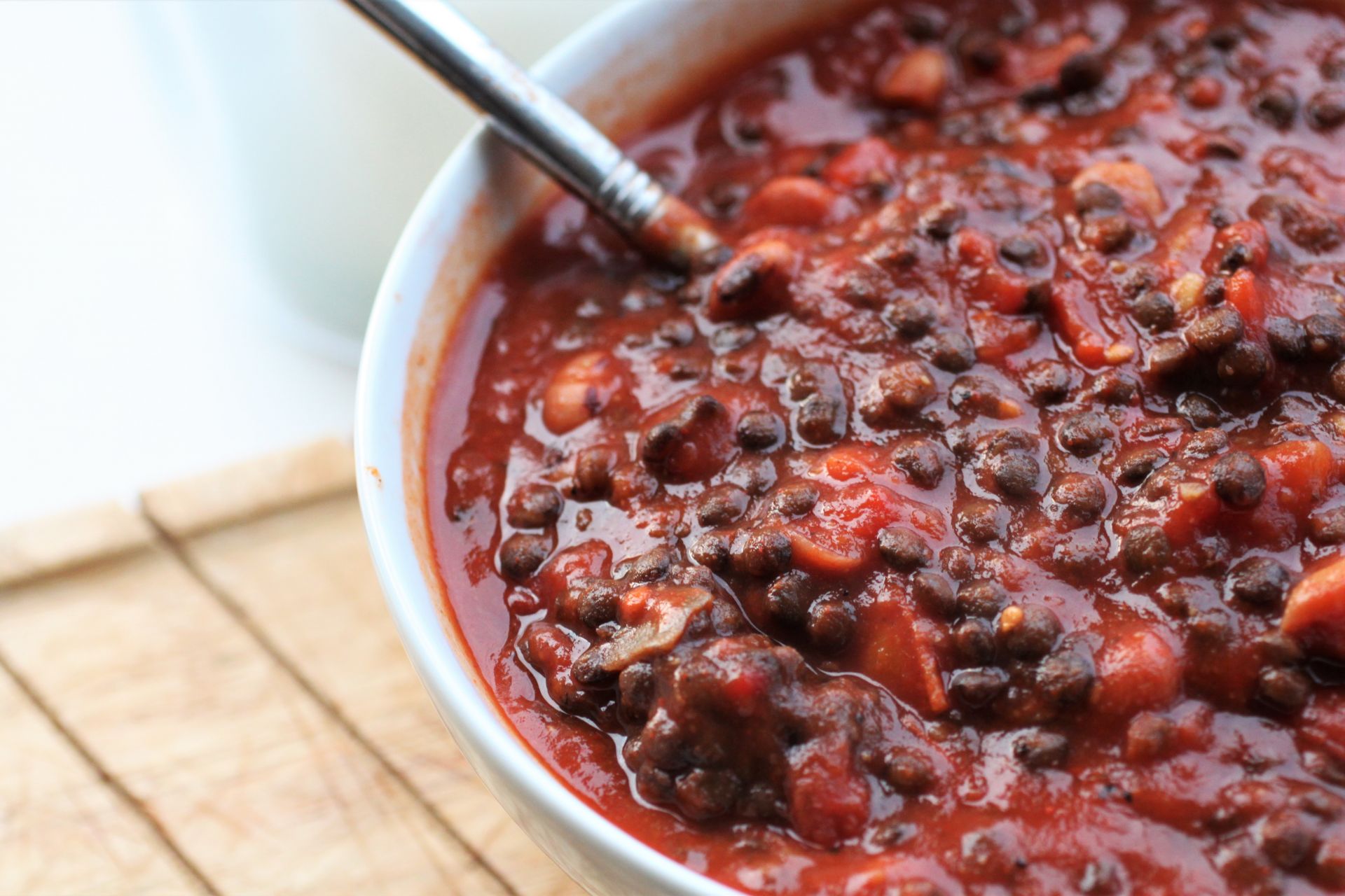 spicy lentil & bean bowl recipe in a while bowl on a wooden tray