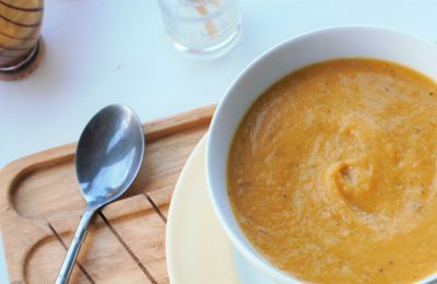 root vegetable soup recipe in a white bowl, on a wooden tray, sat on a white wooden background