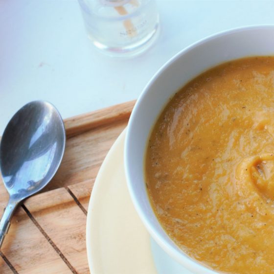 root vegetable soup recipe in a white bowl, on a wooden tray, sat on a white wooden background