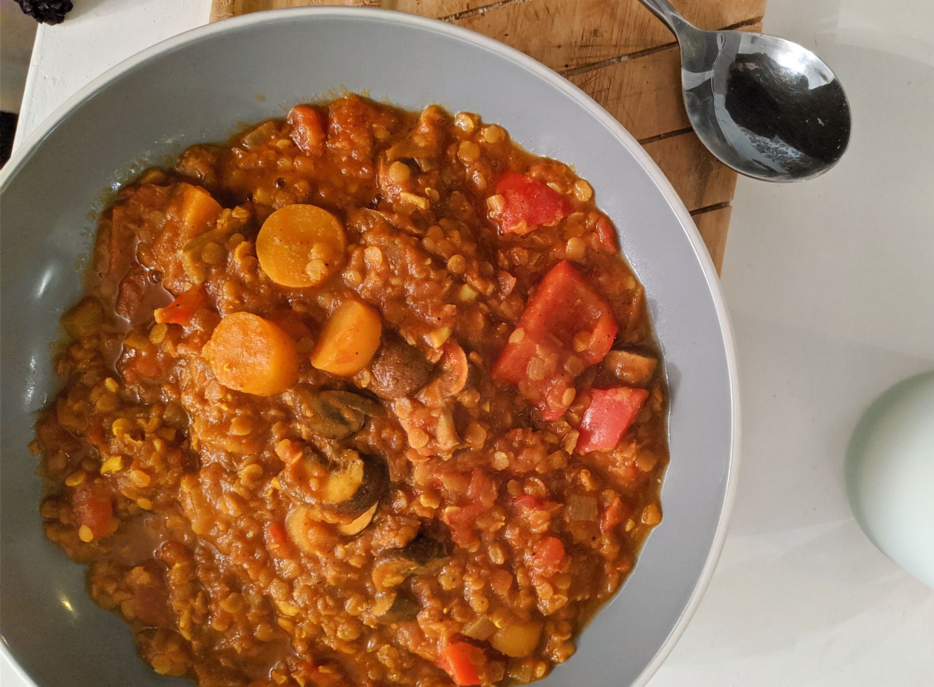 a bowl of lentil curry on a wooden tray, with a spoon
