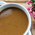 a bowl of butternut squash & red lentil soup on a wooden board, served with a pink rose