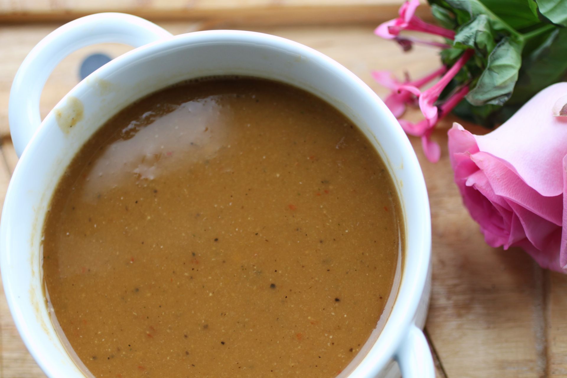 a bowl of butternut squash & red lentil soup on a wooden board, served with a pink rose