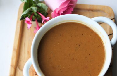 a white bowl of butternut squash & red lentil soup on a wooden tray, with a pink rose