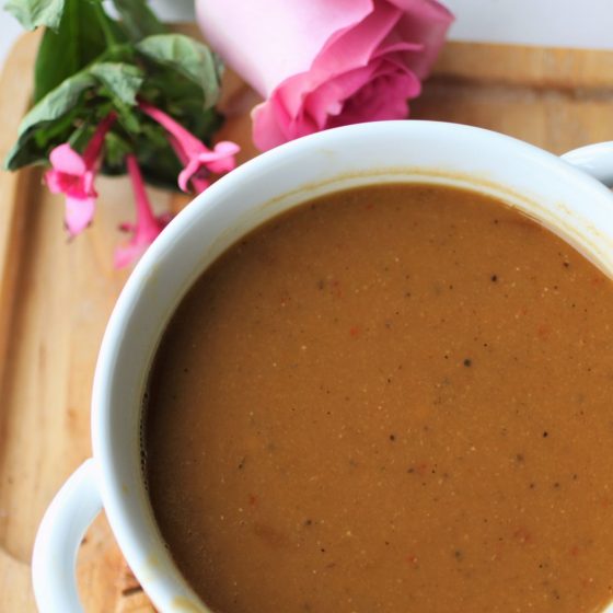 a white bowl of butternut squash & red lentil soup on a wooden tray, with a pink rose