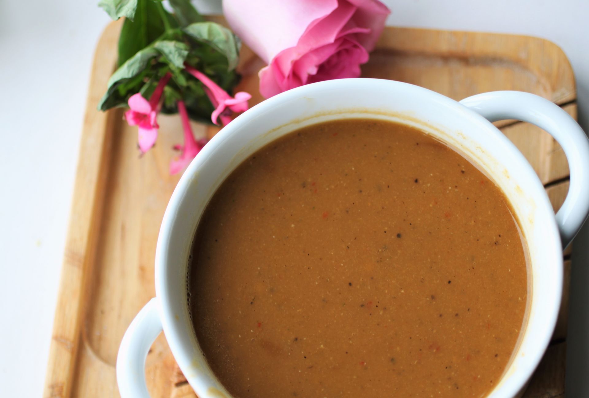 a white bowl of butternut squash & red lentil soup on a wooden tray, with a pink rose