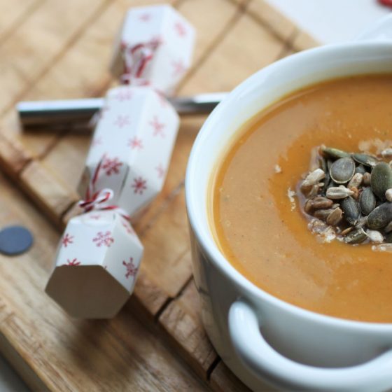 spiced butternut squash soup in a white bowl on a wooden tray, next to a Christmas cracker