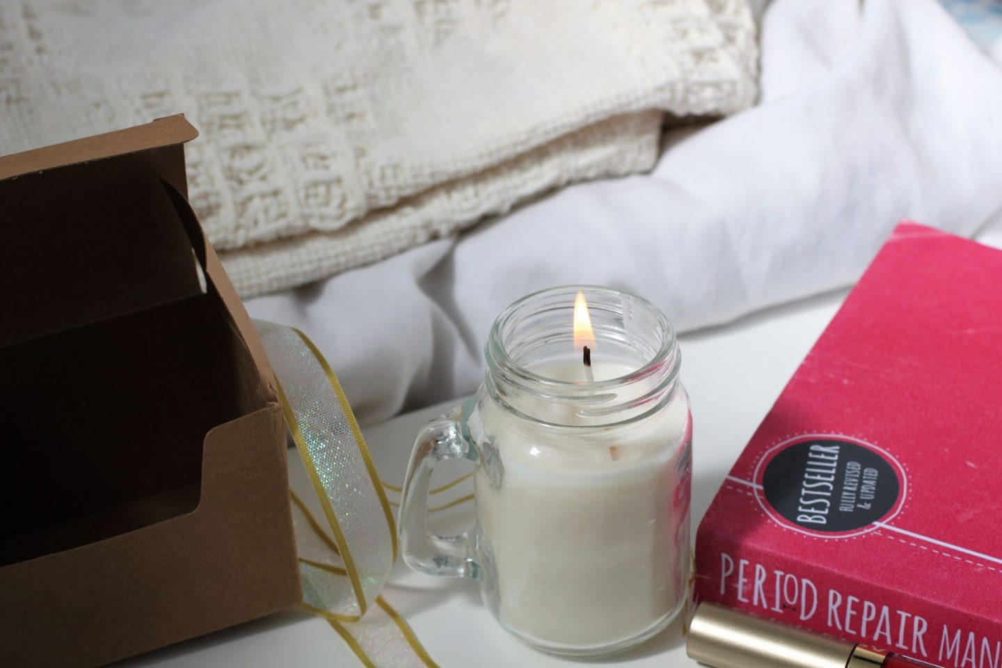 burning candle next to white and cream blankets