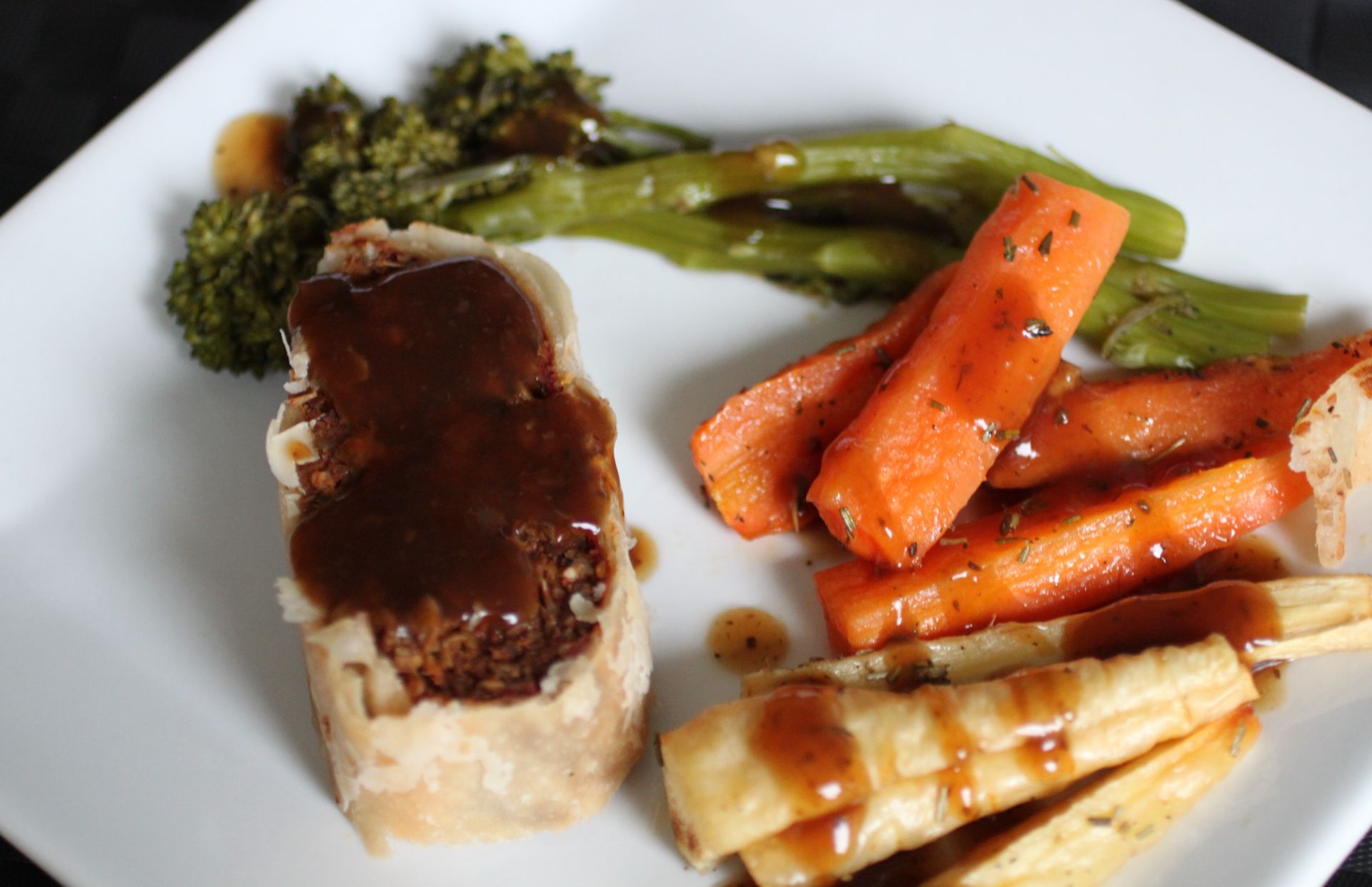 a square white plate with vegan wellington and some vegetables