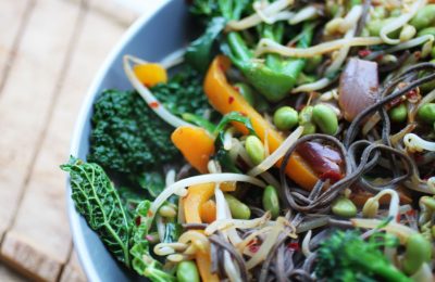 birds eye shot of high protein stir fry in a large grey pasta bowl, sat on a wooden table.