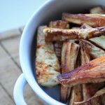 close up shot of a bowl of chilli roasted parsnips in a while bowl, sat on a pale wooden chopping board
