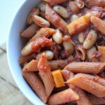 birds eye view of the high protein vegan pasta dish in a white bowl with a wooden tray behind it
