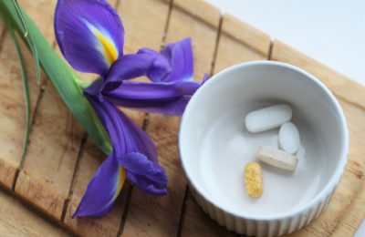 small round white ramakin with 4 pills in it on a wooden board next to an iris