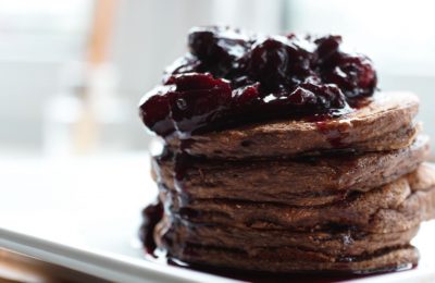 stack of healthy chocolate pancakes on a white plate, topped with berry sauce