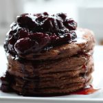 chocolate pancakes on a white plate topped with berries