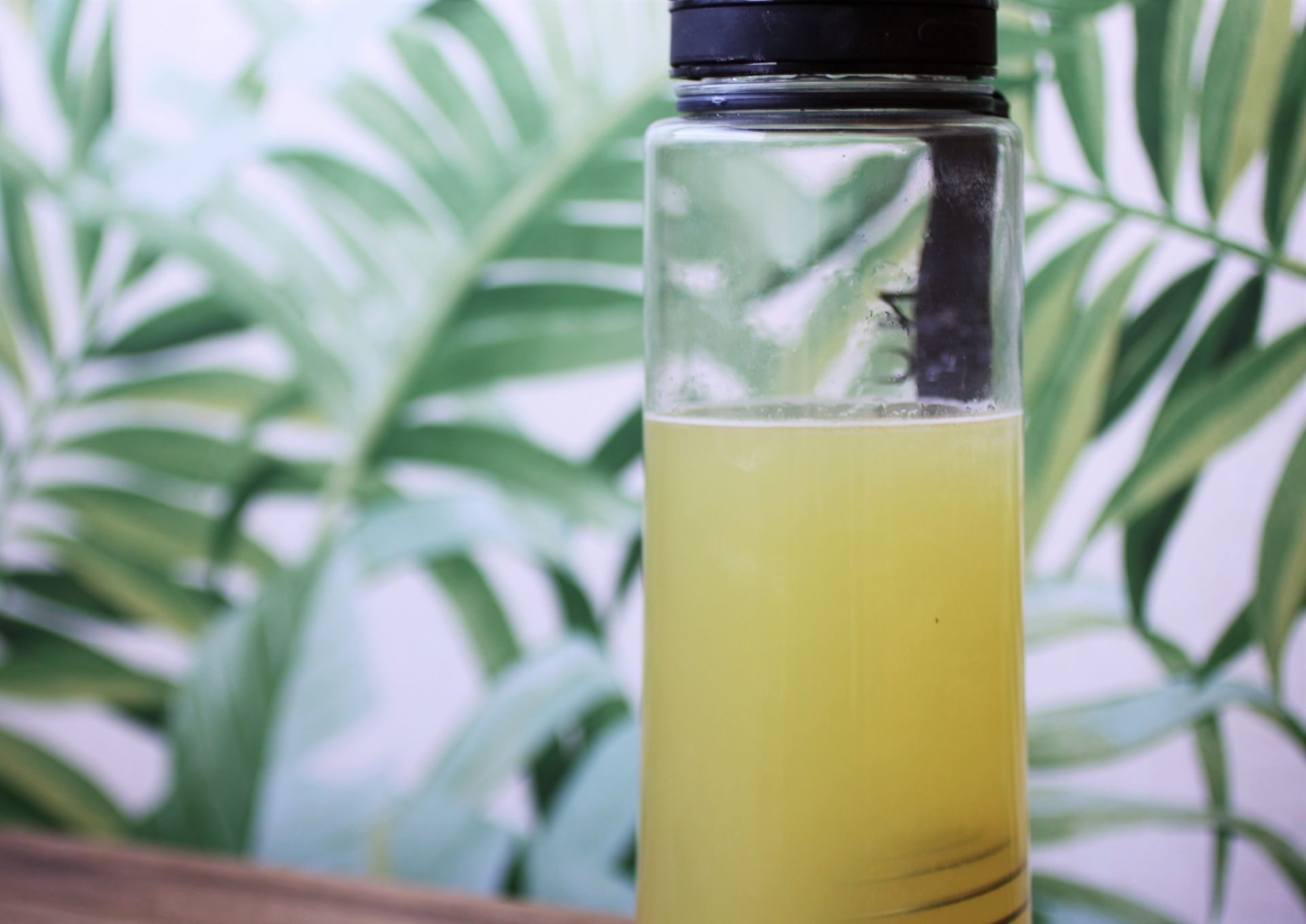 lemon & lime clear protein mixed with water in a protein shaker bottle, against a wall with a green and white leaf print wallpaper