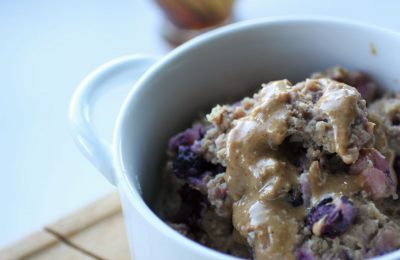 baked oats drizzled with peanut butter in a white bowl with handles on the side, from a sideways angle, bowl is sat on a wooden board