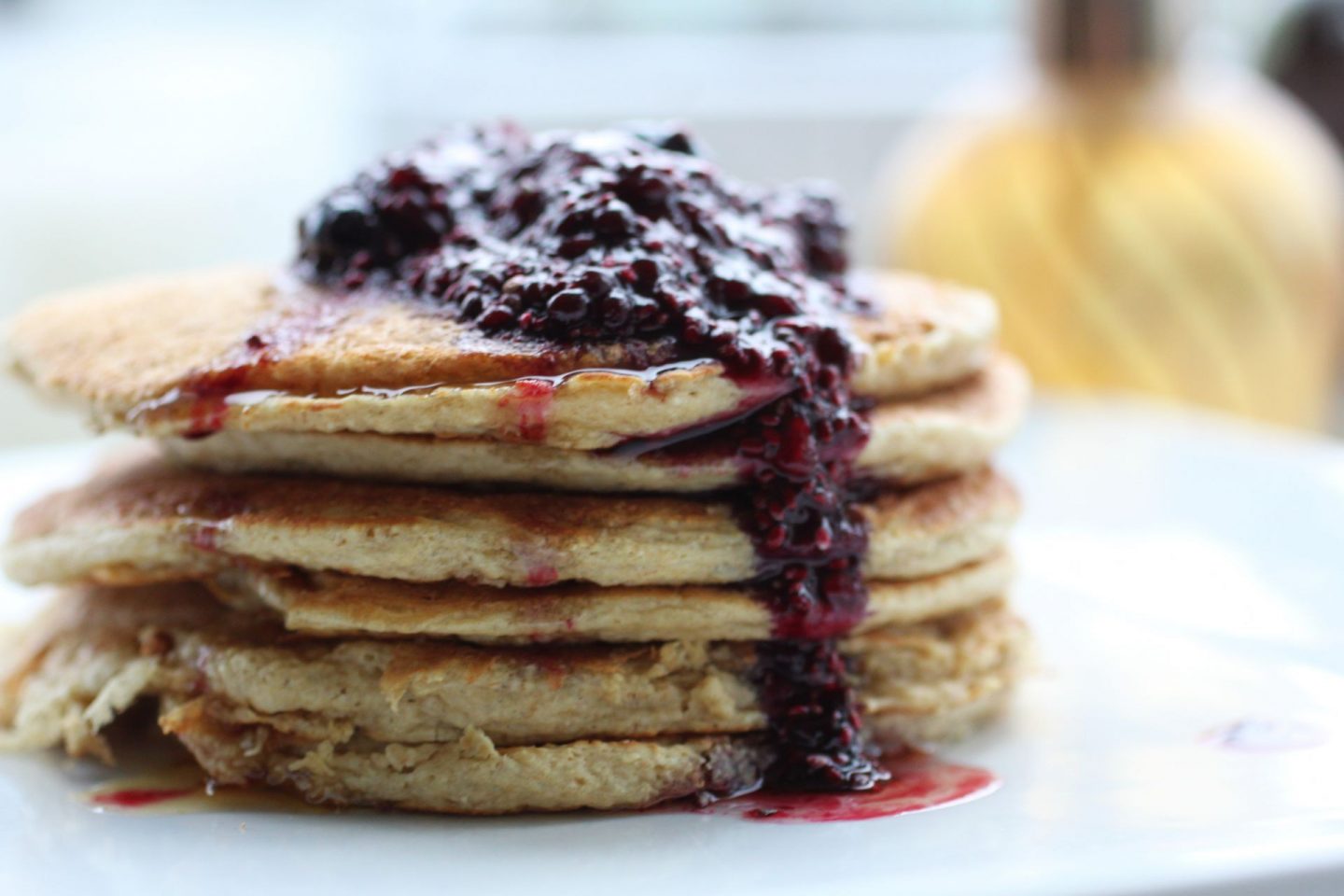 close up shot of vanilla protein pancakes on a white plate with a white background. Pancakes are lightly drizzles with berry sauce and maple syrup