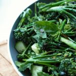 vibrant green salad in a large slate bowl, resting on a wooden tray with a white background behind it.