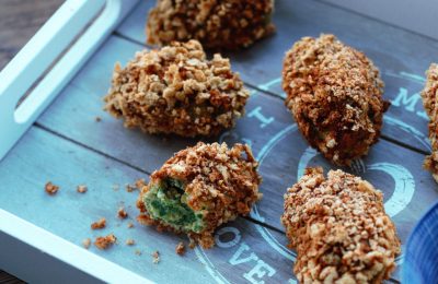 spicy kale nuggets spread out on a grey wooden tray, one nugget bitten in half to show the green inside