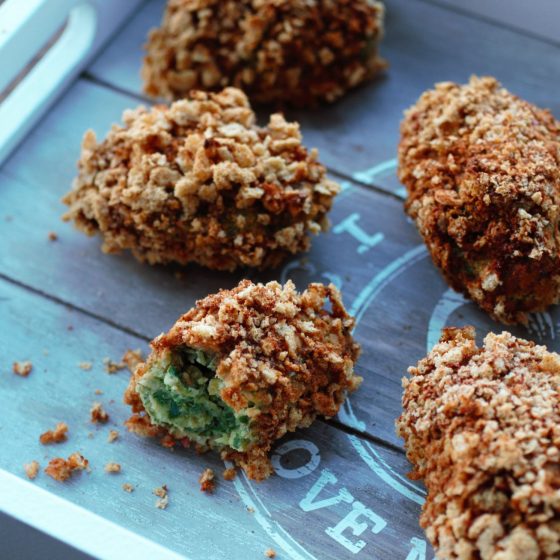 spicy kale nuggets spread out on a grey wooden tray, one nugget bitten in half to show the green inside