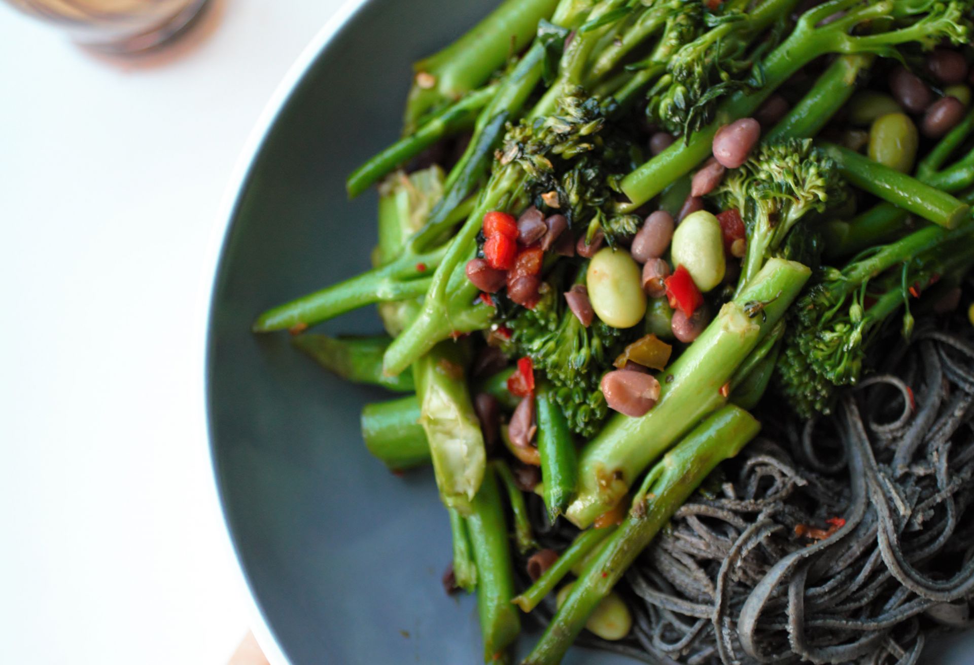 large slate bowl filled with greens and edamame beans and a side of black bean noodles, on a bright white background