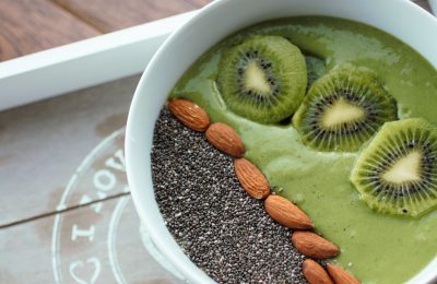 green smoothie bowl in a white bowl with the suggested toppings added. Bowl is on a grey wooden tray with a white trim.