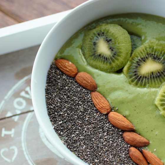 green smoothie bowl in a white bowl with the suggested toppings added. Bowl is on a grey wooden tray with a white trim.
