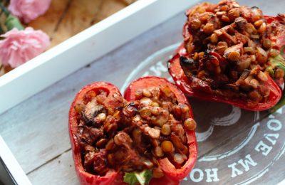 lentil stuffed peppers on a grey wooden tray with white edges and flowers in the background
