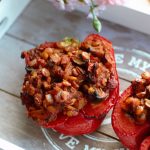 lentil stuffed peppers on a grey wooden tray with some pink flowers over the edge of the tray, shot from above