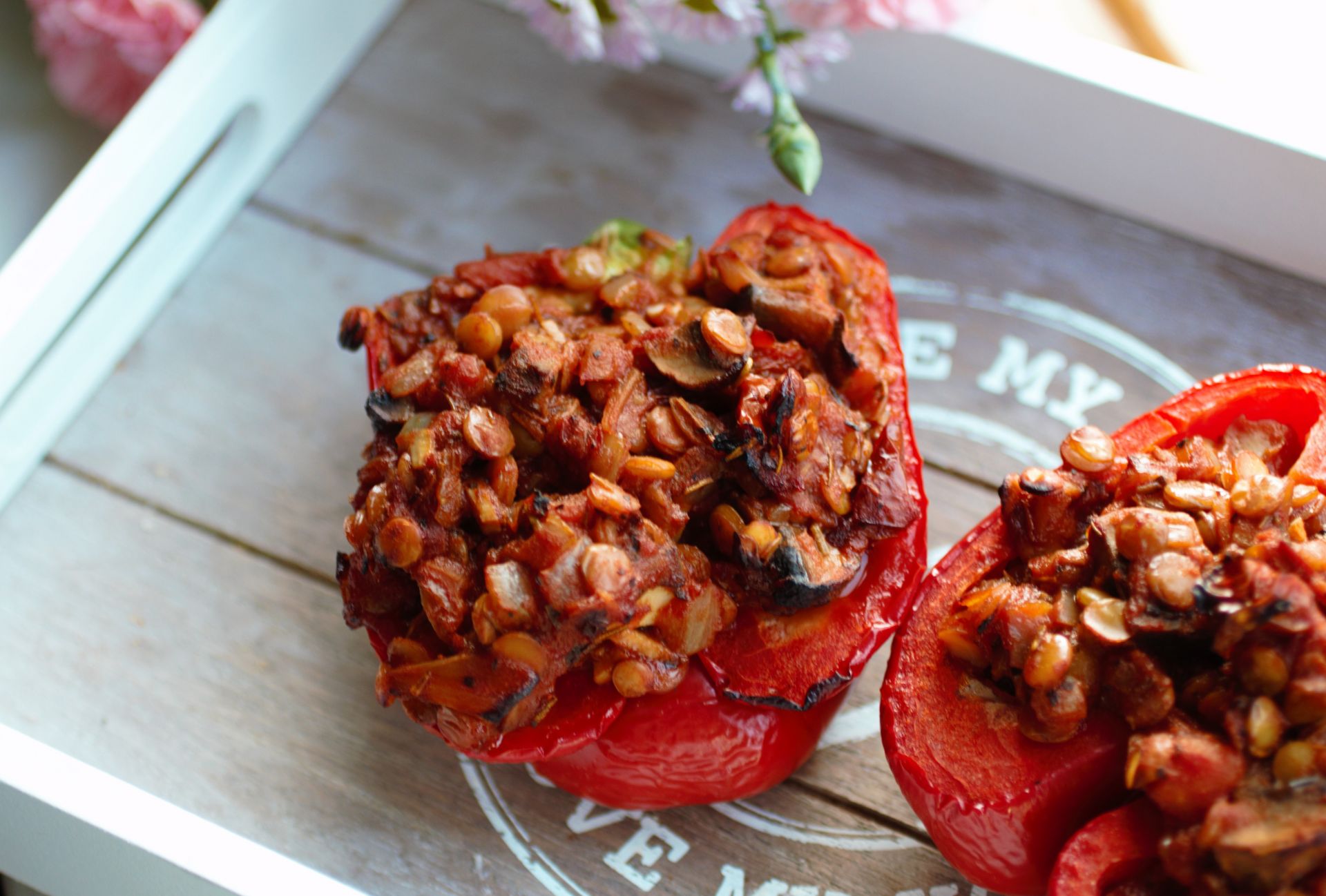 lentil stuffed peppers on a grey wooden tray with some pink flowers over the edge of the tray, shot from above