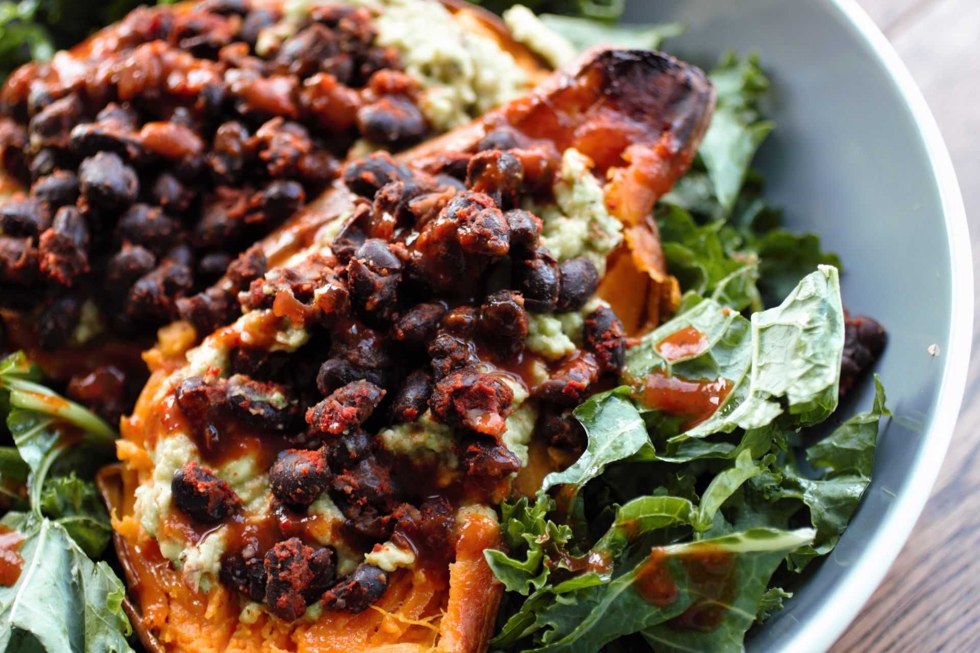 Mexican stuffed sweet potatoes in a grey bowl - close up shot of the black beans/ guacamole filling