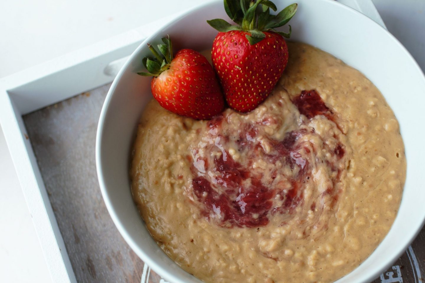 peanut butter jelly oatmeal in a white bowl with some strawberries, the bowl is on a grey wooden tray, at on a white background