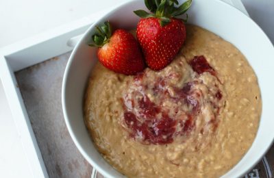 peanut butter jelly oatmeal in a white bowl with some strawberries, the bowl is on a grey wooden tray, at on a white background