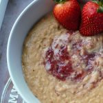 peanut butter oats in a white bowl with strawberry jam swirled through and fresh strawberries on top
