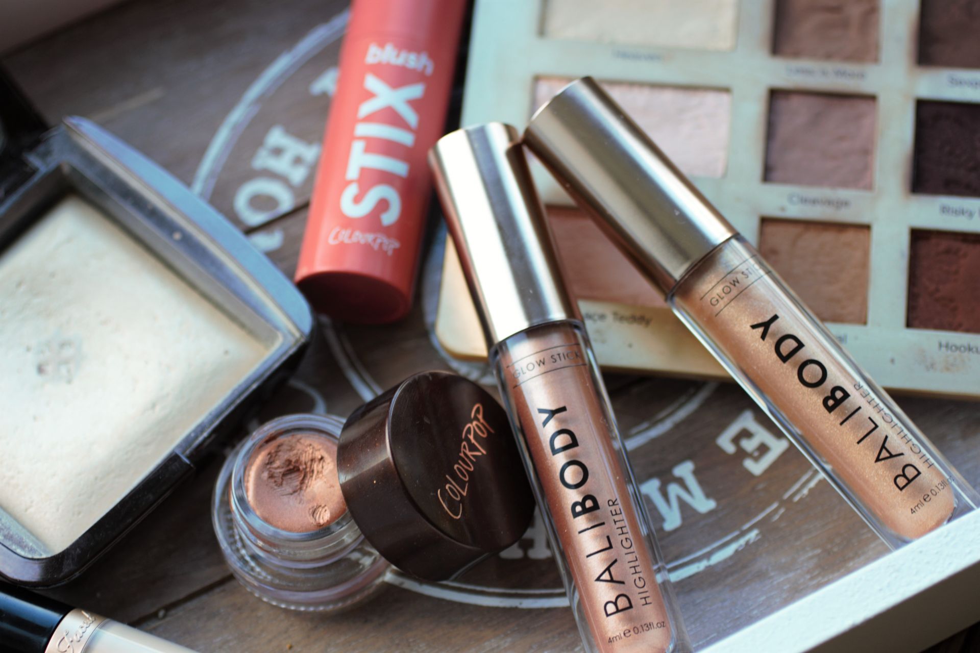 two bali body highlighter sticks on a wooden tray with other makeup