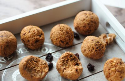 grey wooden tray with carrot cake energy balls on it, and raisins sprinkled over the tray
