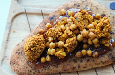 vegan naan bread on a wooden board topped with mango chutney, falafels and roasted chickpeas to make a naan bread pizza.