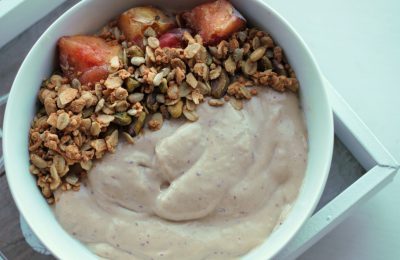 peaches & cream smoothie bowl in a white bowl, topped with some granola and peach chunks. Bowl is on a grey tray against a white background