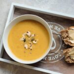 bowl of pumpkin soup on a grey tray with bread