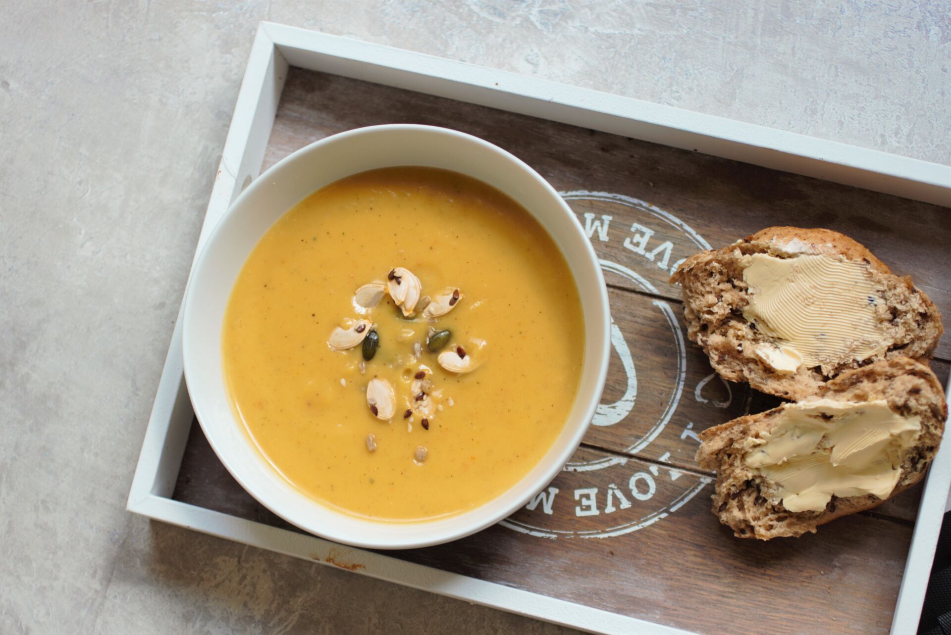 bowl of pumpkin soup on a grey tray with bread