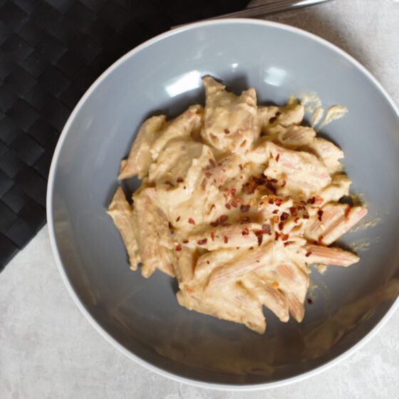 vegan pumpkin alfredo recipe in a grey pasta bowl placed on a white and grey background