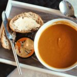 bowl of soup on a tray with bread and a butter dish