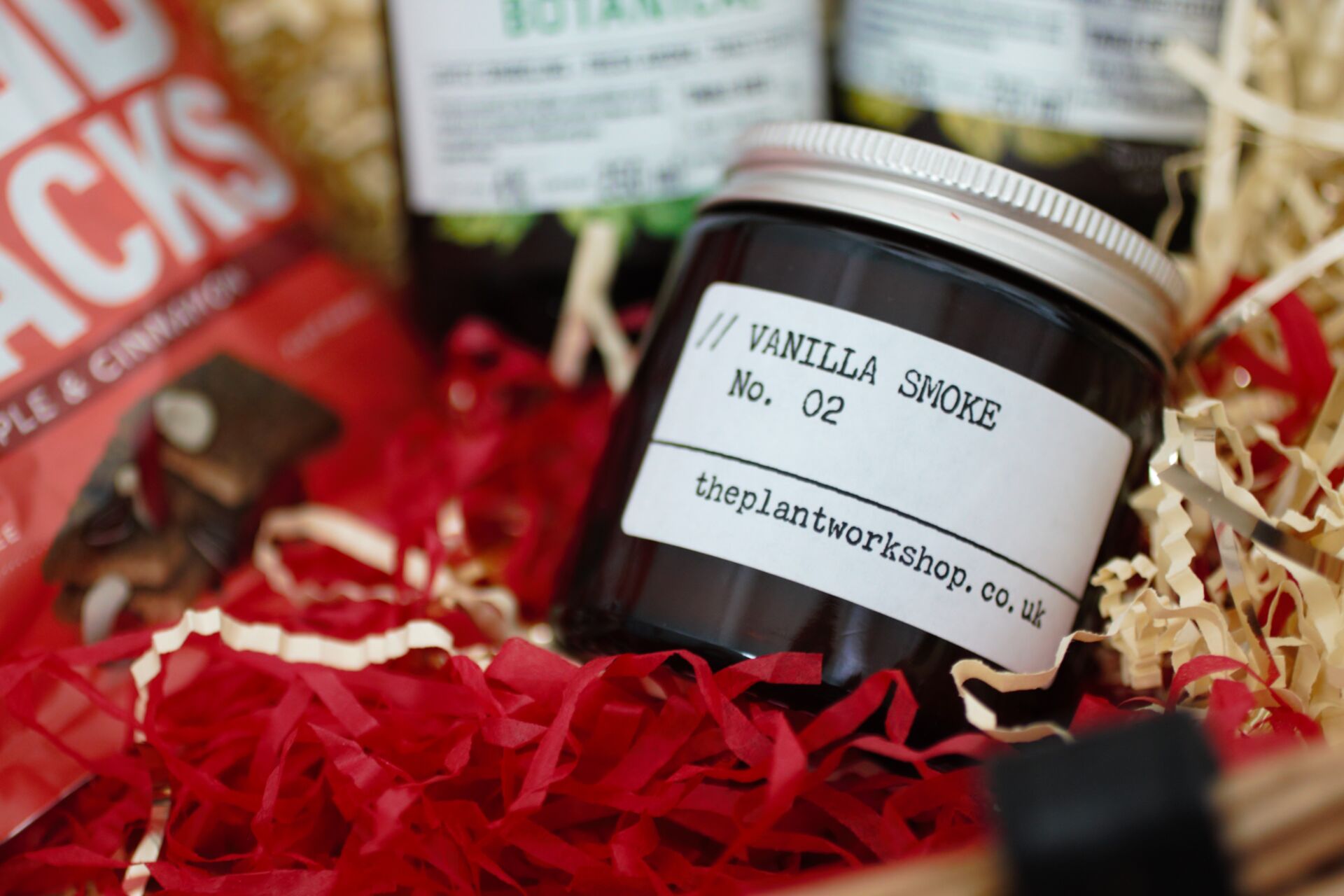 a small candle jar in the hamper with a few other products surrounding it