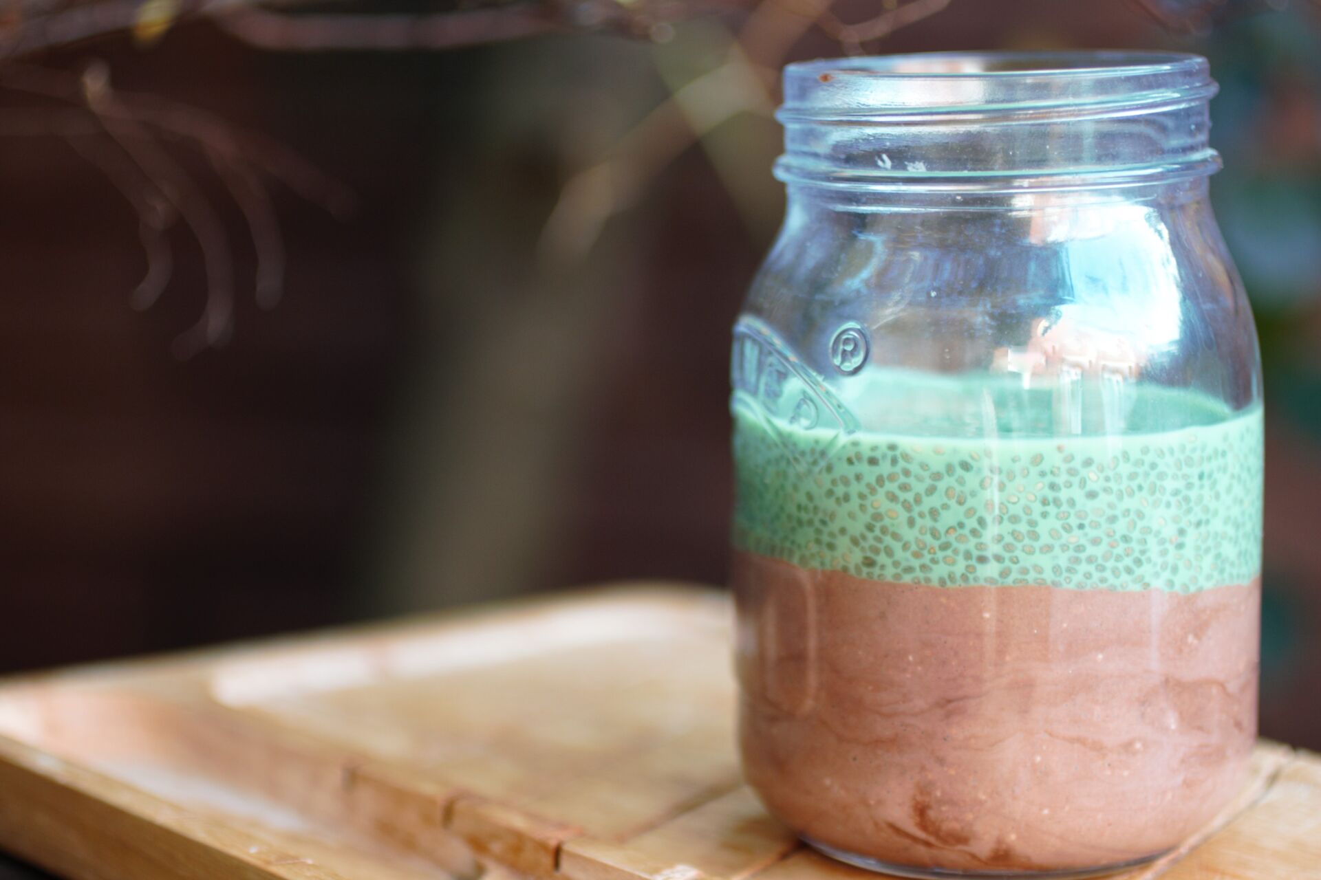 a jar of mint chocolate overnight oats on a wooden tray placed on a garden bench